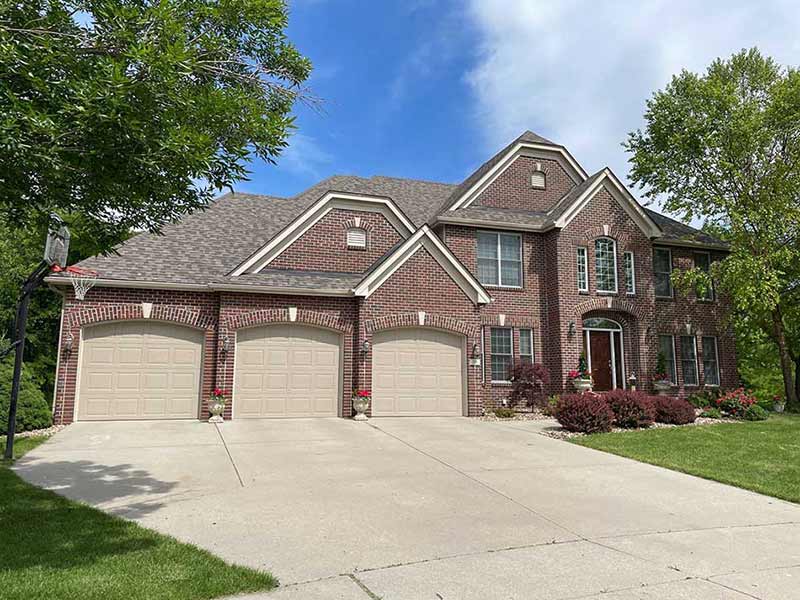 Front view of a large mid-class home with brick siding and a new gray shingle roof worked on by American Dream Exteriors